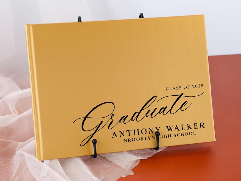 May include: A gold-colored graduation guest book with the text "Graduate" in a black cursive font. The book also includes the text "Class of 2025", "Anthony Walker", and "Brooklyn High School".