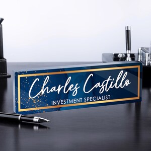 May include: A blue and gold desk nameplate with the text "Charles Castillo, Investment Specialist".