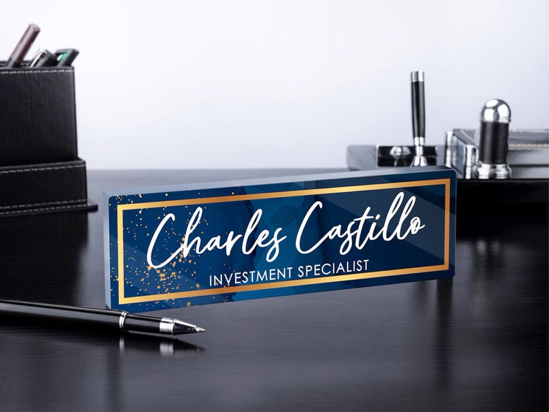 May include: A blue and gold desk nameplate with the text "Charles Castillo, Investment Specialist".