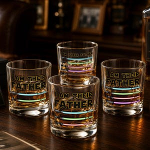 May include: Four clear whiskey glasses with the text "I AM THEIR FATHER" in black. Each glass has a colorful, horizontal light saber design with names. The glasses are filled with amber liquid, likely whiskey.