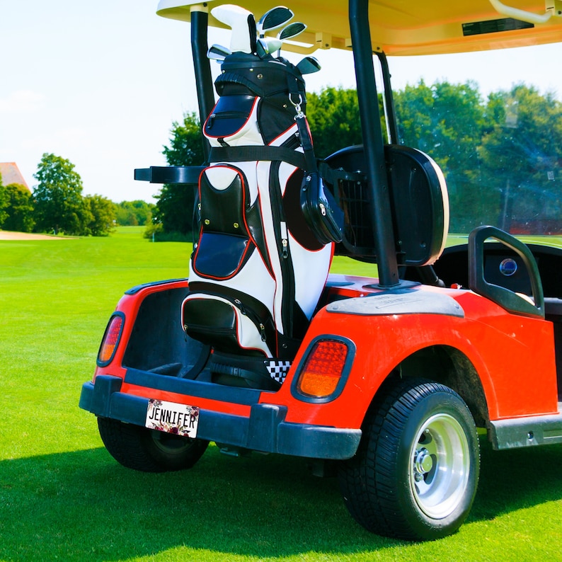 May include: A red golf cart with a black and white golf bag in the back. The golf cart has a license plate that says "Jennifer".