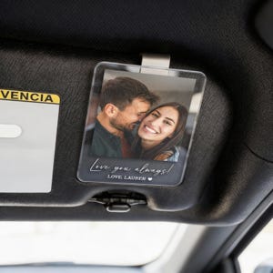 May include: Clear acrylic car visor photo holder with a printed photo of a smiling couple. The holder has the text "Love you always!" and "LOVE, LAUREN" in a handwritten style font.