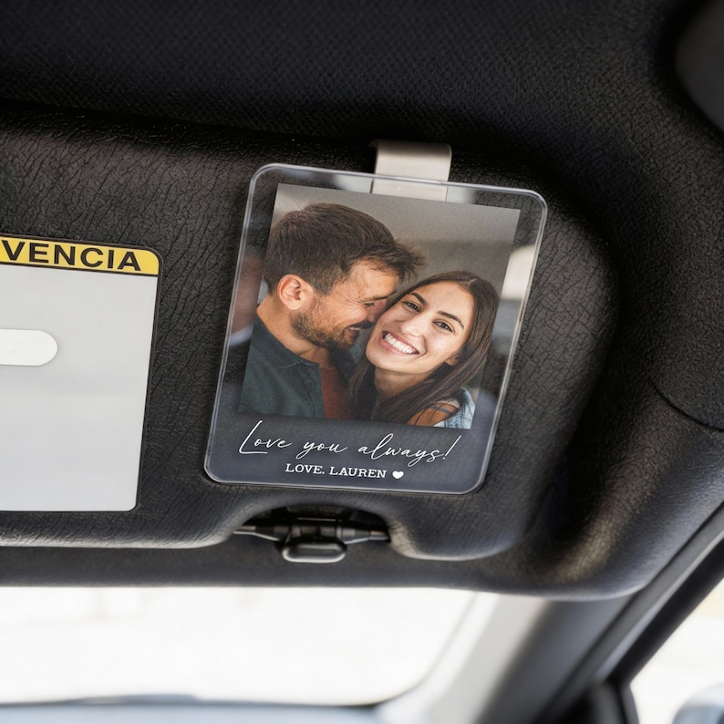 May include: Clear acrylic car visor photo holder with a printed photo of a smiling couple. The holder has the text "Love you always!" and "LOVE, LAUREN" in a handwritten style font.
