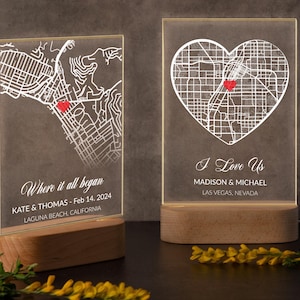 May include: Two illuminated map art pieces on wooden bases. One features a map outline with a red heart, the text "Where it all began", and location details. The other has a heart-shaped map with "I Love Us" and location details.