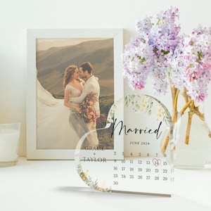 Puede incluir: Un calendario de acr&iacute;lico transparente en forma de coraz&oacute;n con un dise&ntilde;o floral y las palabras "Casado" y "Junio 2024". El calendario tiene un coraz&oacute;n rojo marcando el 14.
