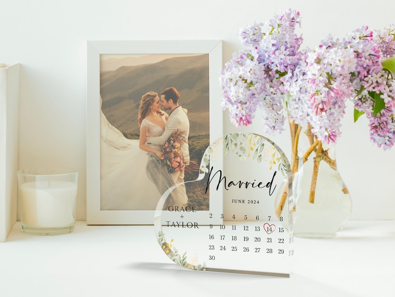 Puede incluir: Un calendario de acr&iacute;lico transparente en forma de coraz&oacute;n con un dise&ntilde;o floral y las palabras "Casado" y "Junio 2024". El calendario tiene un coraz&oacute;n rojo marcando el 14.
