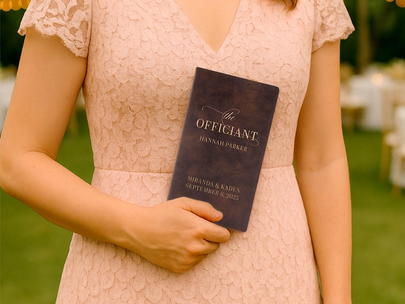 May include: A dark brown wedding program held by a person wearing a pink lace dress. The program reads "the Officiant" with the names "Hannah Parker", "Miranda & Kaden", and the date "September 6, 2025".