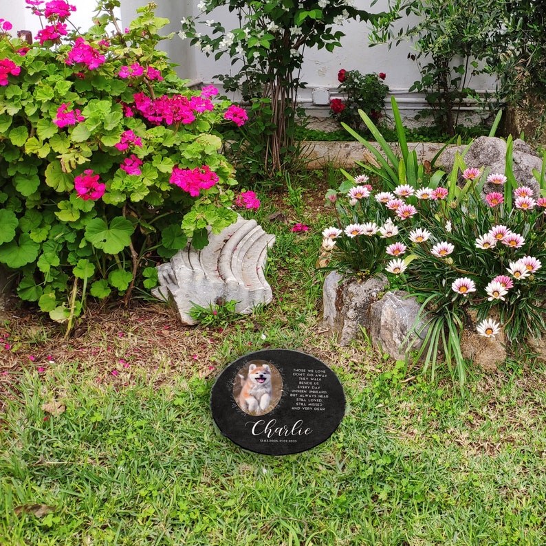 May include: A black granite memorial stone with a photo of a brown and white dog and a poem about those we love. The text reads "Those we love don't go away, they walk beside us every day. Unseen, unheard, but always near, still loved, still missed and very dear." The stone also has the name "Charlie" and the dates "12/18/2013 - 01/13/2020".