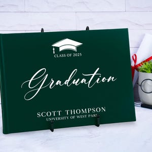 May include: A dark green graduation guest book with a white graduation cap and the text "Class of 2025" and "Graduation". The book also has the name "Scott Thompson" and "University of West Paris" printed on it.