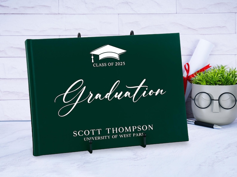 May include: A dark green graduation guest book with a white graduation cap and the text "Class of 2025" and "Graduation". The book also has the name "Scott Thompson" and "University of West Paris" printed on it.