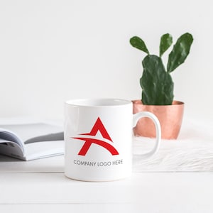 May include: White ceramic mug with a red stylized letter A logo and the text "COMPANY LOGO HERE" printed on the front.