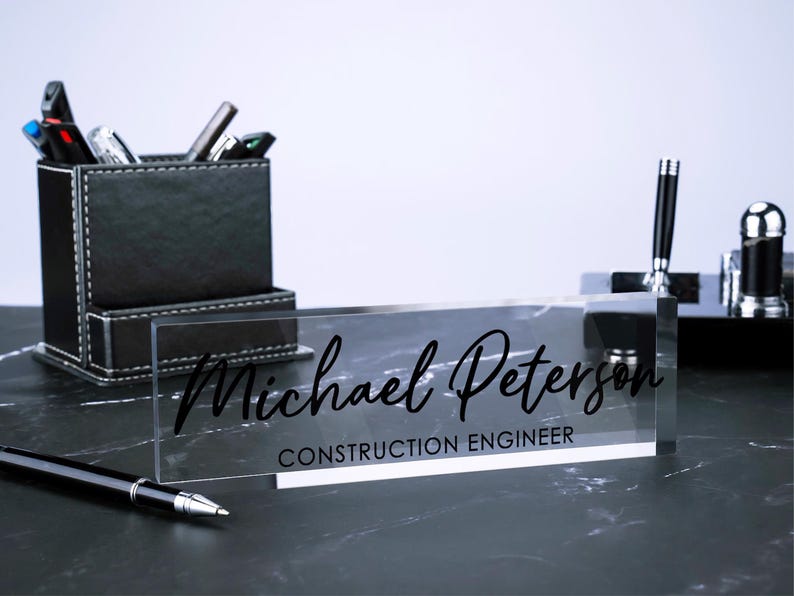 May include: A clear acrylic desk nameplate with black text that reads "Michael Peterson, Construction Engineer".