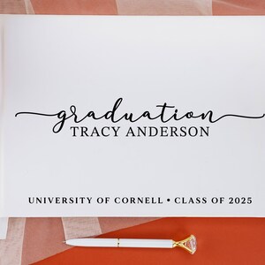 May include: White graduation guest book with the text "graduation TRACY ANDERSON UNIVERSITY OF CORNELL CLASS OF 2025" printed on the front.
