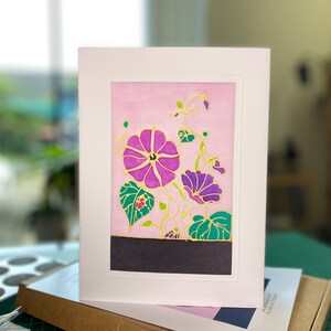 Pode incluir: Um cart&atilde;o de felicita&ccedil;&otilde;es floral rosa e roxo com detalhes dourados. O cart&atilde;o apresenta uma pintura em estilo aquarela de flores com folhas e videiras verdes.