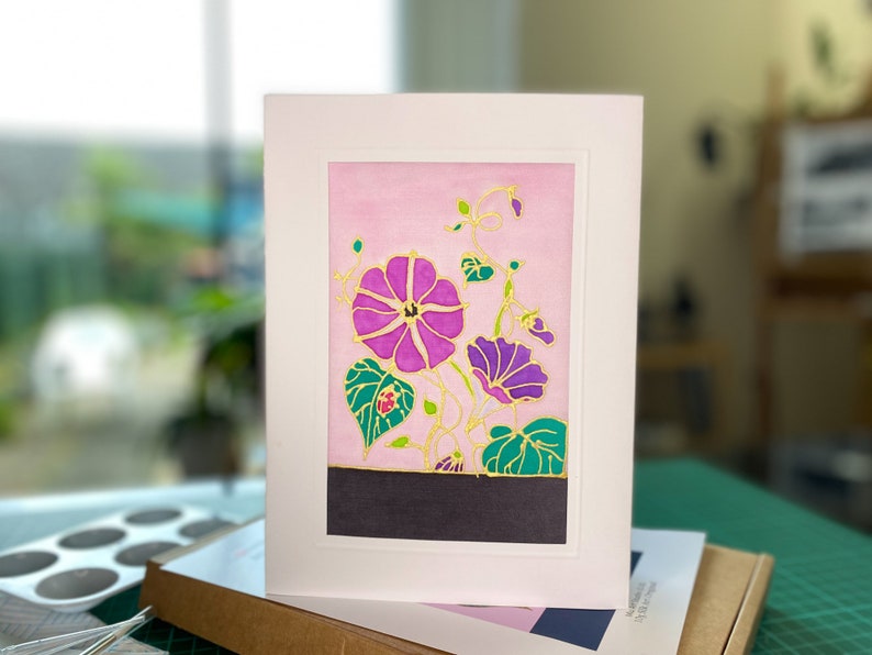 Pode incluir: Um cart&atilde;o de felicita&ccedil;&otilde;es floral rosa e roxo com detalhes dourados. O cart&atilde;o apresenta uma pintura em estilo aquarela de flores com folhas e videiras verdes.