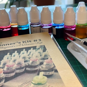 May include: A beginner's silk painting kit with 10 bottles of dye in various colors, a paintbrush, and a palette. The kit includes a guide titled "Beginner's Kit #3 Journey Beyond A Basic Kit".