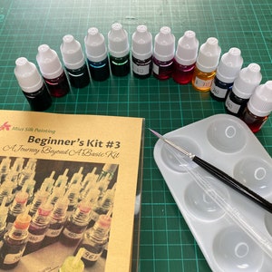 May include: A beginner's silk painting kit with 12 bottles of dye in various colors, a small paint palette, and a paintbrush. The kit includes a guidebook titled "Beginner's Kit #3: A Journey Beyond A Basic Kit".