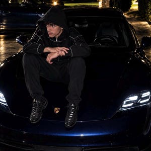 May include: A dark blue sports car with a Porsche emblem on the bonnet. The vehicle features sleek, aerodynamic lines and bright LED headlights. The car has a glossy finish that reflects the surrounding ambient light in a nighttime setting.
