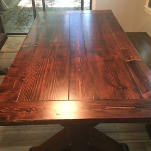 May include: A large, dark wood dining table with a rectangular top and a thick, sturdy base. The table has a rich, dark brown finish and a smooth, polished surface.