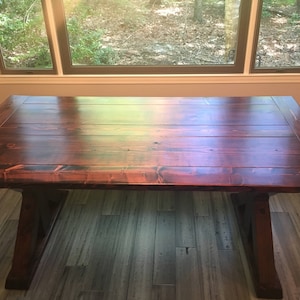 May include: A dark wood dining table with a rectangular top and a trestle base. The table has a rich, reddish-brown finish and a smooth, polished surface.