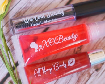 May include: Three tubes of lip gloss with different brand names. The tubes are red, clear, and pink. The lip glosses are labeled "XO Beauty", "All Things Beauty", and "Un Cool Beauty Organic Mascara".