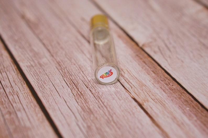 May include: A clear glass roller bottle with a gold cap and a white label with the word "Rainbow" in rainbow colors.