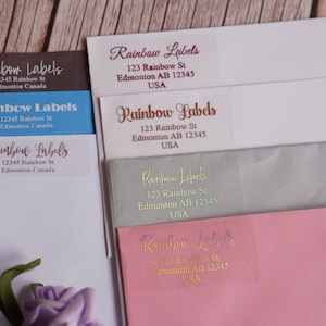 Puede incluir: Primer plano de varios sobres de diferentes colores con etiquetas que dicen "Rainbow Labels" e incluyen una dirección. Las etiquetas están impresas en diferentes colores y fuentes.