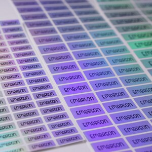May include: A sheet of iridescent holographic stickers with the name "Emerson" printed on each sticker. The stickers are arranged in rows and columns.