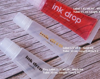 May include: Three tubes of "Ink Drop" ink, each with a different color. The "Tanned Red" tube is filled with red ink, the "Gold Ink" tube is filled with clear ink, and the "Sugar Red" tube is filled with clear ink. The "Tanned Red" tube is 3.5 inches long.