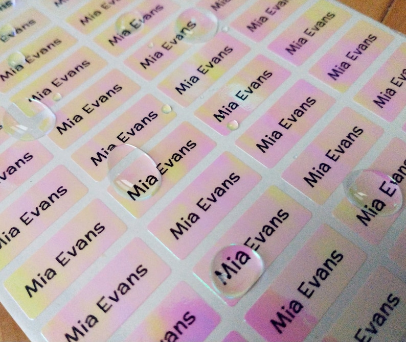 May include: A sheet of colorful, iridescent name labels with the name "Mia Evans" printed on each label. The labels are rectangular and have a glossy finish.