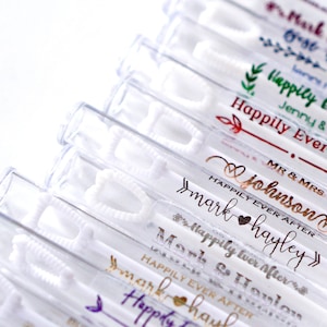 May include: Clear plastic bubble wands with white wands and personalized text in various metallic colors. The text includes names and the phrase "Happily Ever After", perfect for weddings and celebrations.