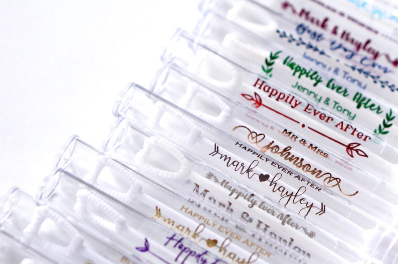May include: Clear plastic bubble wands with white wands and personalized text in various metallic colors. The text includes names and the phrase "Happily Ever After", perfect for weddings and celebrations.