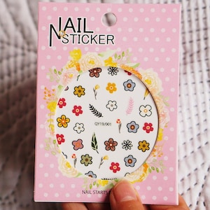 May include: A pink and white package of nail stickers with a floral design. The package says "Nail Sticker" and "Nail Starts Here".
