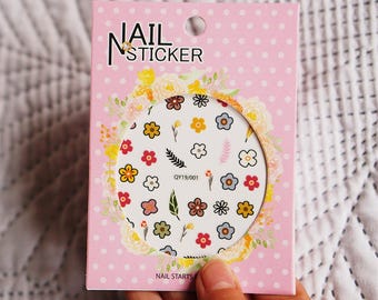 May include: A pink and white package of nail stickers with a floral design. The package says "Nail Sticker" and "Nail Starts Here".