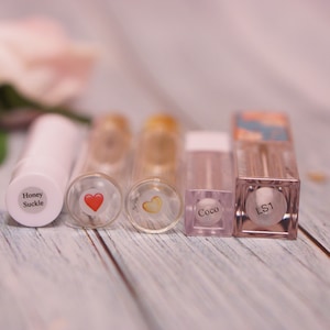 May include: Five clear lip gloss tubes with different labels. The labels include "Honey Suckle", a red heart, a yellow heart, "Coco", and "LS1".