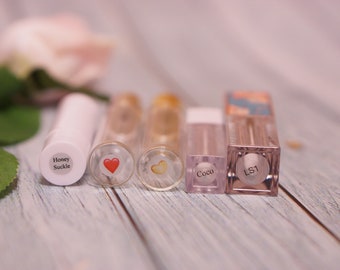 May include: Five clear lip gloss tubes with different labels. The labels include "Honey Suckle", a red heart, a yellow heart, "Coco", and "LS1".
