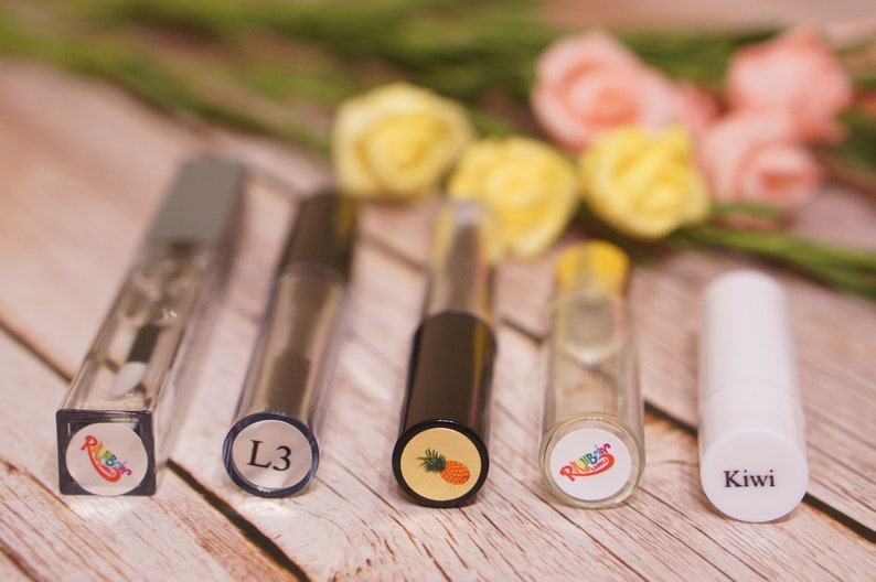 May include: Five small glass bottles with colorful labels. The labels have different designs, including a pineapple, a kiwi, and the word "L3".