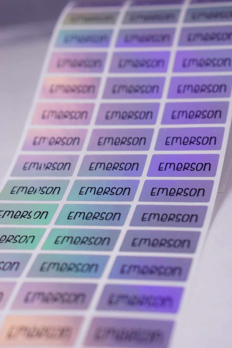 May include: A sheet of iridescent holographic stickers with the name "Emerson" printed on each sticker. The stickers are arranged in rows and columns, with the name "Emerson" repeated on each sticker.