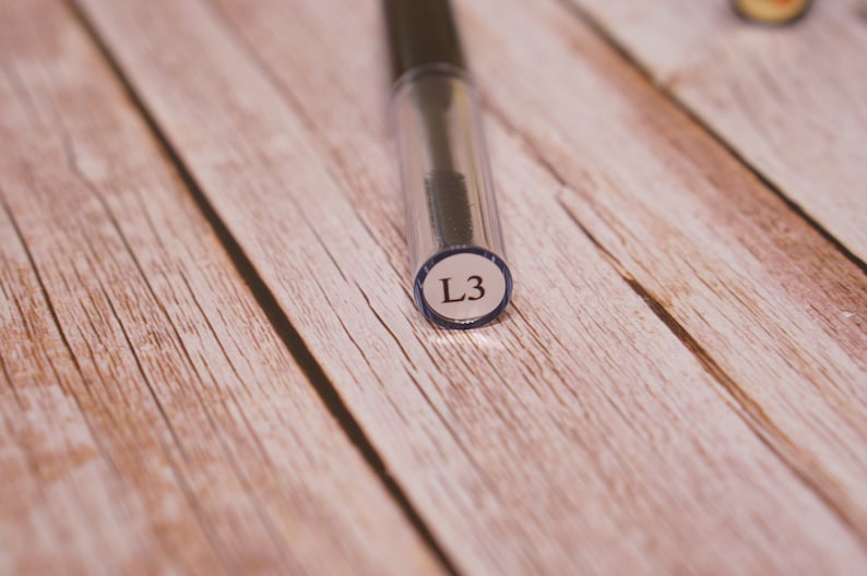 May include: A close-up of a clear plastic tube with a black brush inside. The tube has a white label with the text "L3" on it.