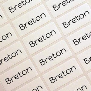 May include: A sheet of rectangular white adhesive labels arranged in a grid pattern. Each individual label features the word Breton printed in a simple black sans-serif font. The labels are uniform in size and shape, designed for clear identification.