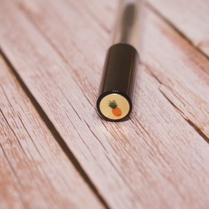May include: A black and gold tube with a pineapple design on the cap.