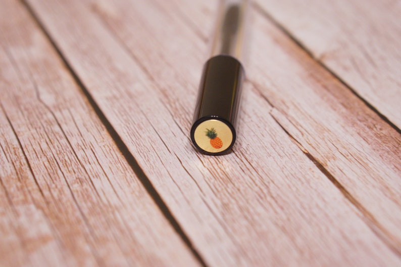 May include: A black and gold tube with a pineapple design on the cap.