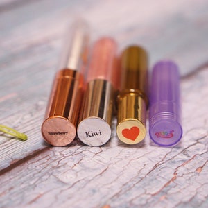May include: Four lip gloss tubes with different coloured caps and labels. The labels read "Strawberry", "Kiwi", a red heart, and "Rainbow".