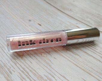 May include: A clear tube with a silver cap containing a pink and shimmery liquid. The tube has the words "ink drop" printed on it.