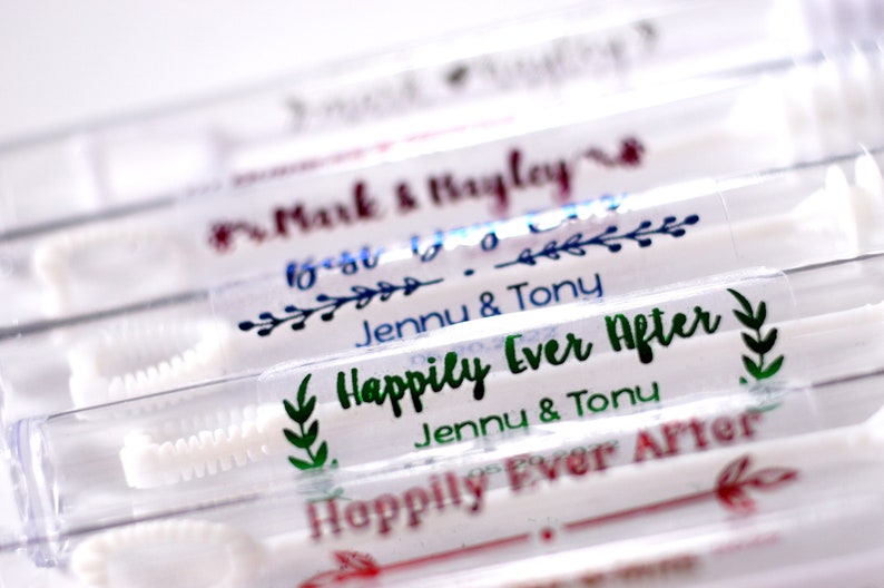 May include: Close-up of several clear bubble wands with personalized labels. The labels feature names and phrases like "Happily Ever After" and "Best Day Ever" in various colors, including green, blue, and red. The wands are arranged in a row.