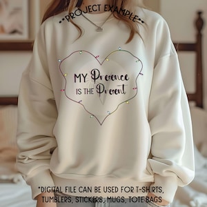 May include: A white sweatshirt with a heart-shaped design featuring a string of colorful lights and the text "My Presence is the Present".