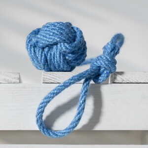 Könnte beinhalten: Ein blauer dekorativer Seeknoten aus Seil. Der Knoten ist rund und liegt neben einer Seilschlaufe, beide in hellblauer Farbe. Die Artikel sind auf einer weißen Oberfläche platziert.