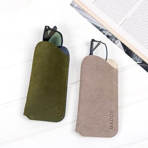 Peut inclure: Deux &eacute;tuis &agrave; lunettes en daim, un vert olive et un taupe, chacun contenant une paire de lunettes. L'&eacute;tui vert olive porte le nom "LIZ" en relief, et l'&eacute;tui taupe porte le nom "MADDY" en relief.