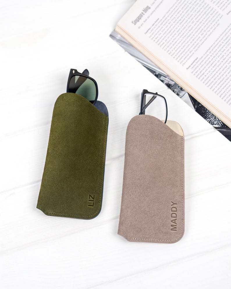Peut inclure: Deux &eacute;tuis &agrave; lunettes en daim, un vert olive et un taupe, chacun contenant une paire de lunettes. L'&eacute;tui vert olive porte le nom "LIZ" en relief, et l'&eacute;tui taupe porte le nom "MADDY" en relief.