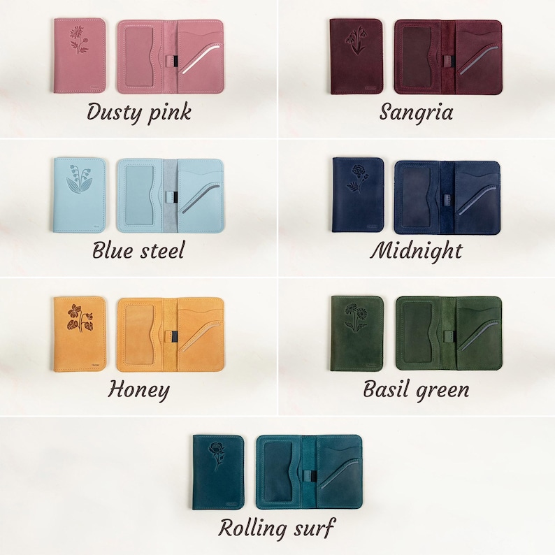 May include: A collection of leather wallets in various colors, including dusty pink, sangria, blue steel, midnight, honey, basil green, and rolling surf. Each wallet features a floral design and the color name is displayed below each set.